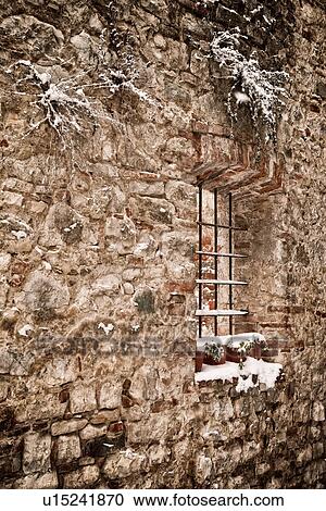 Stock Image - Close up view of stone house facade with iron grate in window opening, on snowy winter morning, MonteCastello di Vibio, Umbria, Italy. Fotosearch