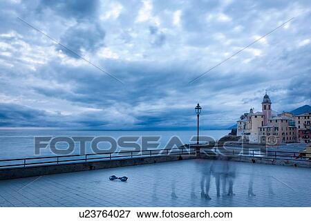 Stock Photo - Deserted terrace of Camogli at dusk with single abandoned skateboard, and motion blur 'ghosts', church tower and buildings, coastline beyond the iron railing, Camogli, Liguria, Italy. Fotosearch