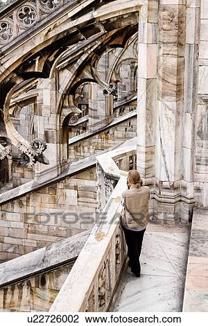 Detail of Milan Duomo rooftop: series of rooftop flying buttresses, elaborate stone carving, with single person seen from behind, aerial desaturated view, Milan Italy View Large Photo Image Stock Image - Detail of Milan Duomo rooftop: series of rooftop flying buttresses, elaborate stone carving, with single person seen from behind, aerial desaturated view, Milan Italy. Fotosearch