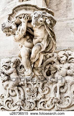 Stock Photography - Detail of Milan Duomo rooftop: elaborate stone carving of two putti supporting statue and frolicking putti in bas-relief, Milan Italy. Fotosearch