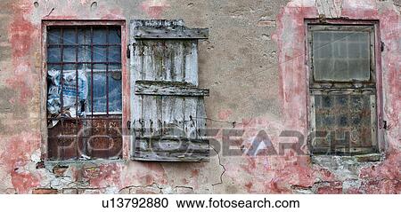 Detail of old derelict warehouse: crumbling pink and red stucco wall, broken window with rusty metal grate. broken wooden shutter hanging, and adjacent window boarded over with green cover, Emilia Romagna, Italy View Large Photo Image Stock Image - Detail of old derelict warehouse: crumbling pink and red stucco wall, broken window with rusty metal grate. broken wooden shutter hanging, and adjacent window boarded over with green cover, Emilia Romagna, Italy. Fotosearch