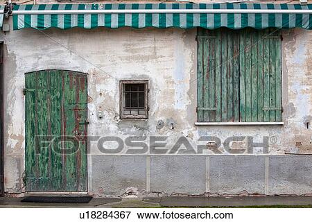 Detail of old stucco house with crumbling facade, green wooden shutter over door with green and white awning, and green wooden shuttered windows, all paint peeling, typical style, Emilia Romagna, Italy View Large Photo Image Stock Photo - Detail of old stucco house with crumbling facade, green wooden shutter over door with green and white awning, and green wooden shuttered windows, all paint peeling, typical style, Emilia Romagna, Italy. Fotosearch