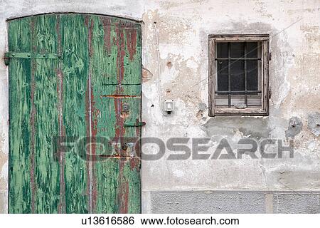 Stock Photograph - Detail of old stucco house with crumbling facade, green wooden shutter over door. metal grate over window, all paint peeling, typical style, Emilia Romagna, Italy. Fotosearch