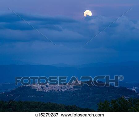 Stock Photo - Full moon rising over hilltop town of Todi in blue twilight with gentle clouds over Tiber valley, hills beyond, Umbria, Italy. Fotosearch