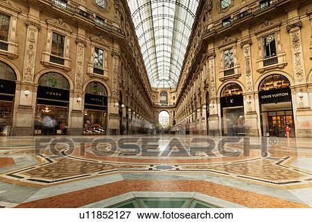 Gallerica Vittorio Emanuele: detail view of central mall area, people shopping, glass and cast iron arched roof with stone carving decoration, Milan Italy View Large Photo Image Stock Photo - Gallerica Vittorio Emanuele: detail view of central mall area, people shopping, glass and cast iron arched roof with stone carving decoration, Milan Italy. Fotosearch