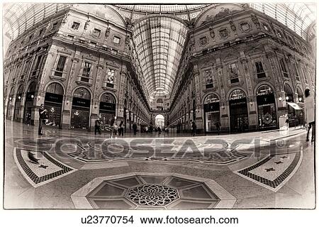 Picture - Gallerica Vittorio Emanuele: wide angle view of central mall area, people shopping, glass and cast iron arched roof with stone carving decoration, mosaic flooring, monochrome view, Milan Italy. Fotosearch
