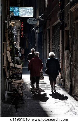 Genoa Centro Storico: narrow alley with fruit and vegetable stand in chiaroscuro light, with women walking, strong shadows, Genova, Italy View Large Photo Image Stock Image - Genoa Centro Storico: narrow alley with fruit and vegetable stand in chiaroscuro light, with women walking, strong shadows, Genova, Italy. Fotosearch