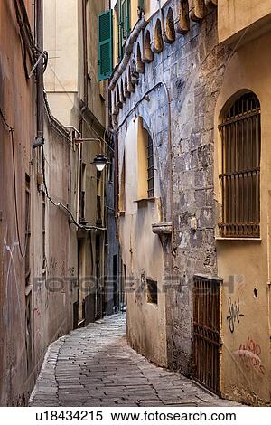 Stock Photography - Genoa Centro Storico: narrow cobbled alleyway with medieval stone facade visible under peeling paint and graffitti covered stucco, Genova, Italy. Fotosearch