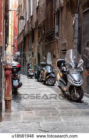 Stock Photo - Genoa Centro Storico: narrow paved alleyway with motorbikes parked along walls of graffitti covered stucco with peeling paint, Genova, Italy. Fotosearch