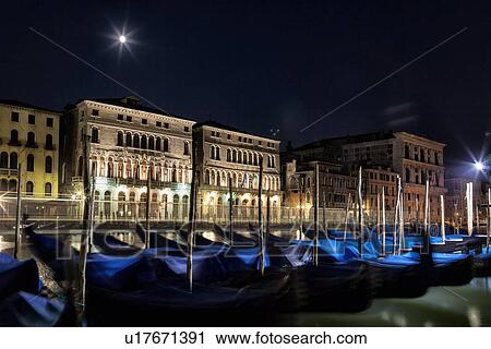 Stock Image - Gondolas rocking on a tranquil Grand canal at nightime in the moonlight with view of ornate Palazzi beyond, Venice Italy. Fotosearch
