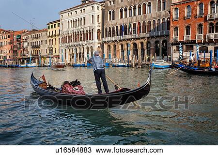 Grand Canal: gondolier rowing single passenger in foreground, ornately decorated palazzi, brightly coloured poles for mooring gondolas, late afternoon golden light, Venice, Italy View Large Photo Image Stock Image - Grand Canal: gondolier rowing single passenger in foreground, ornately decorated palazzi, brightly coloured poles for mooring gondolas, late afternoon golden light, Venice, Italy. Fotosearch
