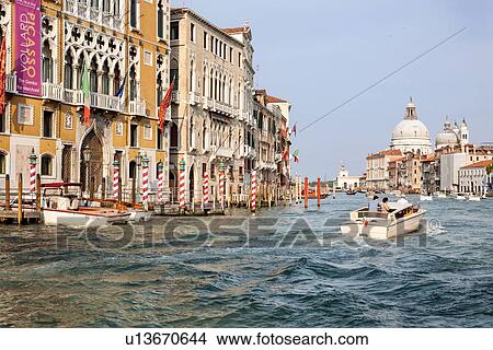 Picture - Grand Canal: ornately decorated palazzi, red and white striped poles for mooring gondolas, motor launch with passengers, Santa Maria della Salute beyond, late afternoon golden light, Venice, Italy. Fotosearch