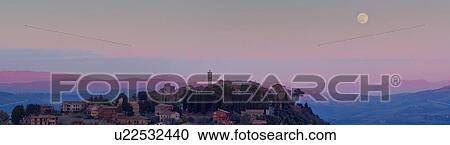 Stock Image - Hilltop medieval town of MonteCastello di Vibio with full moon rising above church and campanile, snowcapped mountains and hills beyond, Umbria, Italy. Fotosearch