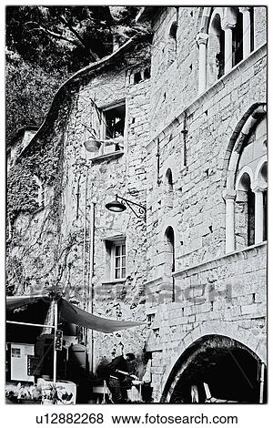 Stock Photo - Man at window with pulley system from kitchen, lowering basket of supplies to restaurant on beach below, old stone building of San Fruttuoso Abbey, monochrome image, Camogli, Liguria, Italy. Fotosearch