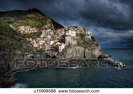 Manarola at sunset: village and fishing harbour lit by sunlight, sweeping black clouds with storm approaching, Cinque Terre, Liguria, Italy View Large Photo Image Stock Photo - Manarola at sunset: village and fishing harbour lit by sunlight, sweeping black clouds with storm approaching, Cinque Terre, Liguria, Italy. Fotosearch