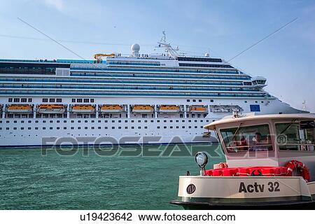 Stock Image - Massive cruise boat in San Marco basin, with approaching ferry boat approaching in foreground, Venice, Italy. Fotosearch