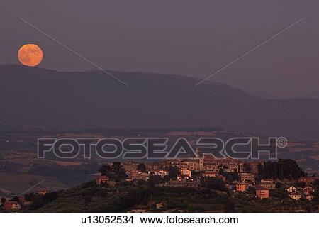 Picture - Medieval hilltop town of MonteCastello di Vibio at sunset, as an orange full moon rises over the hills beyond the Tiber valley, Umbria, Italy. Fotosearch