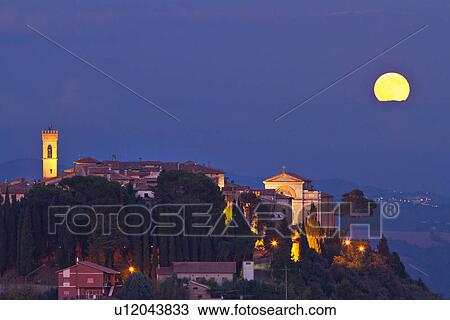 Stock Image - Medieval hilltop town of MonteCastello di Vibio with church and campanile at dusk, as an yellow full moon rises over the hills beyond the Tiber valley, close up view, Umbria, Italy. Fotosearch