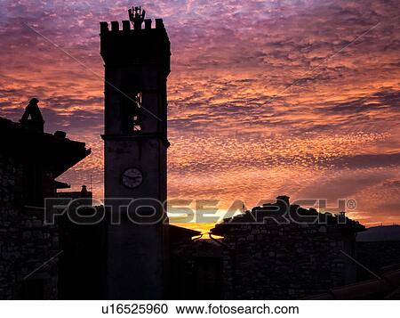 Stock Image - Medieval hilltop town of MonteCastello di Vibio: piazza at dusk, with close up of campanile and old stone buildings silhouetted against amazing ornage purple pink sky, Umbria, Italy. Fotosearch