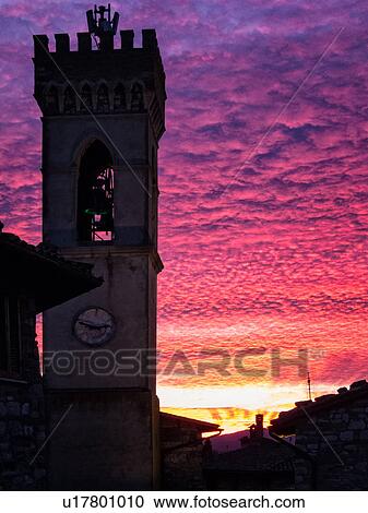 Stock Image - Medieval hilltop town of MonteCastello di Vibio: piazza at dusk, with close up of campanile and old stone buildings silhouetted against amazing ornage purple pink sky, Umbria, Italy. Fotosearch