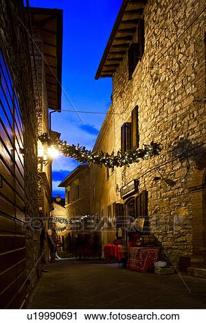 Stock Image - Medieval hilltop town of MonteCastello di Vibio: street at dusk, with night lights, and Christmas garlands strung between the old stone houses, Umbria, Italy. Fotosearch