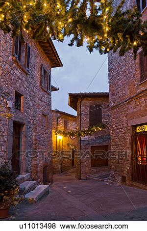 Stock Photo - Medieval hilltop town of MonteCastello di Vibio: street at dusk, with night lights, and Christmas garlands strung between the old stone houses, Umbria, Italy. Fotosearch