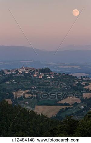 Stock Photo - Medieval hilltop town of MonteCastello di Vibio at sunset, as the pale full moon rises over the hills beyond the Tiber valley, Umbria, Italy. Fotosearch