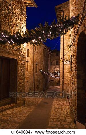 Stock Photo - Medieval hilltop town of MonteCastello di Vibio: street at dusk, with night lights, and Christmas garlands strung between the old stone houses, motion blur of people, Umbria, Italy. Fotosearch
