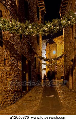 Stock Photography - Medieval hilltop town of MonteCastello di Vibio: street at night, with night lights, and Christmas garlands strung between the old stone houses, motion blur of people, Umbria, Italy. Fotosearch