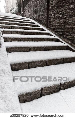 Stock Image - Medieval street - stone house and stairway entrance, covered with snow in early dawn light, desaturated view, MonteCastello di Vibio, Umbria, Italy. Fotosearch