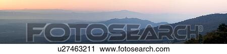 Stock Image - Panorama view of Tiber valley at sunrise with hills silhouetted purple by valley mist, with hilltop town of Todi and spire of San Fortunato outlined, gentle pink sky, Umbria, Italy. Fotosearch
