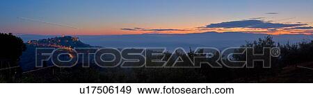 Panorama view of Tiber valley at sunrise with hills silhouetted purple by valley mist, with night lights of hilltop town of MonteCastello di Vibio, against pink and blue sky, Umbria, Italy View Large Photo Image Stock Photo - Panorama view of Tiber valley at sunrise with hills silhouetted purple by valley mist, with night lights of hilltop town of MonteCastello di Vibio, against pink and blue sky, Umbria, Italy. Fotosearch