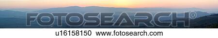Stock Image - Panorama view of Tiber valley with Tiber river at sunrise with hills silhouetted purple by valley mist, with hilltop town of Todi and spire of San Fortunato outlined, gentle pink-orange sky, Umbria, Italy. Fotosearch