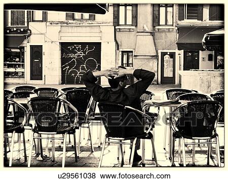 Stock Photo - Quiet moment: back view of a man sitting at an open cafe with buildings and graffitti covered doorway beyond, Campo Santa Margherita, monochrome image, Venice, Italy. Fotosearch