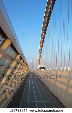 Reggio Emilia bridge by Calatrava, detail showing curved hoop design and suspension wires and oncoming truck, with pedestrian sidewalk, second bridge beyond, against blue sky at sunset, Emilia Romagna, Italy View Large Photo Image Picture - Reggio Emilia bridge by Calatrava, detail showing curved hoop design and suspension wires and oncoming truck, with pedestrian sidewalk, second bridge beyond, against blue sky at sunset, Emilia Romagna, Italy. Fotosearch