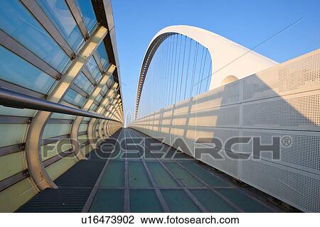 Reggio Emilia bridge by Calatrava, detail showing curved hoop design and suspension wires, with pedestrian sidewalk, second bridge beyond, against blue sky at sunset, Emilia Romagna, Italy View Large Photo Image Stock Image - Reggio Emilia bridge by Calatrava, detail showing curved hoop design and suspension wires, with pedestrian sidewalk, second bridge beyond, against blue sky at sunset, Emilia Romagna, Italy. Fotosearch