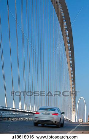 Reggio Emilia bridge by Calatrava, detail showing curved hoop design and suspension wires with cars passing in foreground, and second bridge beyond, against blue sky in late afternoon, Emilia Romagna, Italy View Large Photo Image Stock Photograph - Reggio Emilia bridge by Calatrava, detail showing curved hoop design and suspension wires with cars passing in foreground, and second bridge beyond, against blue sky in late afternoon, Emilia Romagna, Italy. Fotosearch