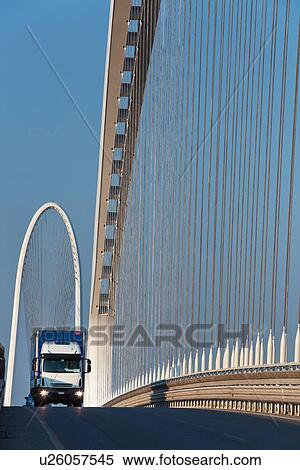 Stock Photography - Reggio Emilia bridge by Calatrava, detail showing curved hoop design and suspension wires with oncoming truck in foreground, and second bridge beyond, against blue sky in late afternoon, Emilia Romagna, Italy. Fotosearch