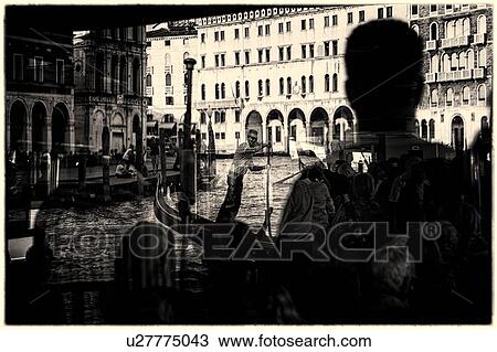 Stock Image - Rialto Bridge reflections: monochrome image of passengers reflected in glass windows of ferry, Rialto bridge and gondolier framed beyond, Venice, Italy. Fotosearch