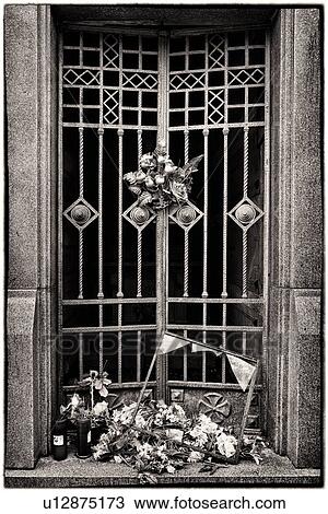 Stock Image - Roses tied to metal wrought iron gate at cemetery, broken glass frame and heap of flowers on step, monochrome image, Monterosso al Mare, Cinque Terre, Liguria, Italy. Fotosearch