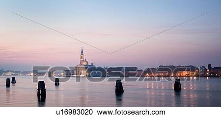 Stock Image - San Giorgio Maggiore as seen at dawn with lights of the Giudecca, and pink calm water reflected from dawn sky, Venice, Italy. Fotosearch