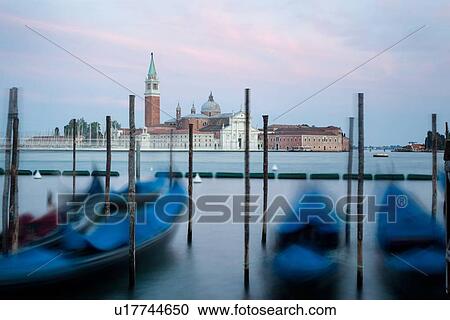 Stock Image - San Giorgio Maggiore: view across San Marco basin with moored gondolas moving on the water at sunset, Venice, Italy. Fotosearch