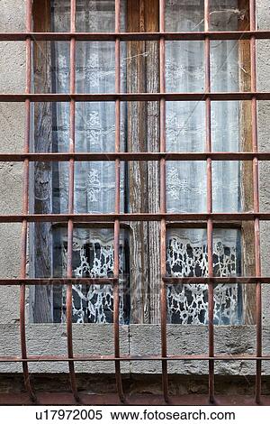 Stock Photography - Square glass window with metal grate iin front, rwhite lace curtain hanging, with surrounding stone wall, medieval village, close up detail view Umbria, Italy. Fotosearch