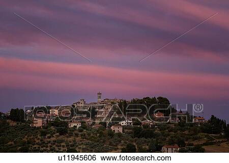 Stock Photograph - Sunset view of medieval hilltop town of MonteCastello di Vibio. stone houses and belltower, olive groves on slope below, with pink and blue twilight sky, Umbria, Italy. Fotosearch