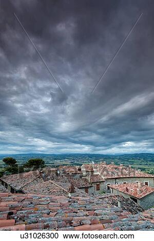 Stock Image - Terrace view over red tiled rooftops to Tiber valley and hills beyond, with dramatic storm clouds gathering overhead, Montecastello di Vibio, Umbria, Italy. Fotosearch