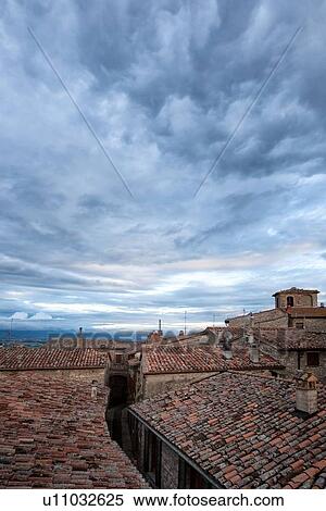 Stock Photography - Terrace view over red tiled rooftops to Tiber valley and hills beyond, with dramatic storm clouds gathering overhead, Montecastello di Vibio, Umbria, Italy. Fotosearch