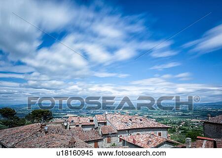 Stock Photography - Terrace view over red tiled rooftops to Tiber valley and hills beyond, with cloud motion in blue sky, Montecastello di Vibio, Umbria, Italy. Fotosearch