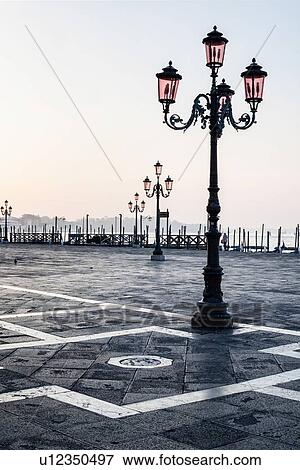 The Molo San Marco in front of Doge's Palace at dawn with empty piazza, row of traditonal wrought iron lamps, view of gondola station and San Marco basin beyond, Venice, Italy View Large Photo Image Stock Photo - The Molo San Marco in front of Doge's Palace at dawn with empty piazza, row of traditonal wrought iron lamps, view of gondola station and San Marco basin beyond, Venice, Italy. Fotosearch
