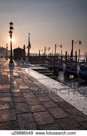 Stock Photo - The Molo San Marco in front of Doge's Palace at dawn, with row of traditonal wrought iron lamps, view of gondola station and San Marco basin beyond, Venice, Italy. Fotosearch