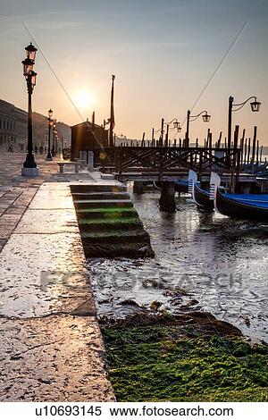 Stock Photography - The Molo San Marco in front of Doge's Palace at dawn with steps down to the gondola station, row of traditional wrought iron lamps, and San Marco basin beyond, Venice, Italy. Fotosearch